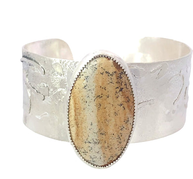 Silver cuff bracelet with a large oval stone on a white background