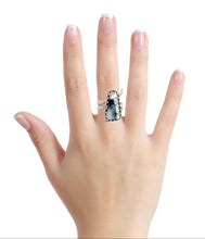 Load image into Gallery viewer, Hand wearing a ring with a dendritic opal gem design on a white background