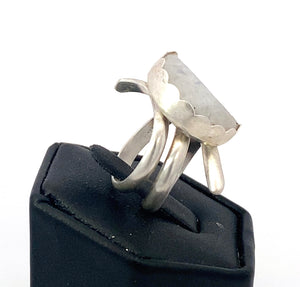 Silver ring with a large stone on a black stand against a white background