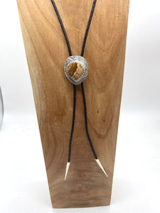 Bolo tie with a decorative clasp on a wooden block against a white background