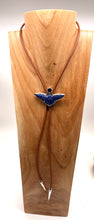 Load image into Gallery viewer, A brown cord bolo tie necklace with a blue and silver lapis gemstonne eagle  displayed on a wooden stand.