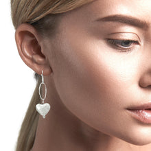 Load image into Gallery viewer, Close-up of a woman wearing a silver heart-shaped earring on a neutral background