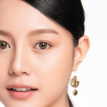 Load image into Gallery viewer, Close-up of a woman wearing gold earrings with a plain background