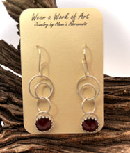Load image into Gallery viewer, Pair of silver earrings with red garnes on a display card, set against a natural wood background.