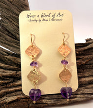 Load image into Gallery viewer, A pair of dangling earrings displayed on a cream jewelry card that reads 'Wear a Work of Art Jewelry by Alene's Adornments.' The earrings have gold fill hooks and textured gold metal.r- with faceted amethyst gems