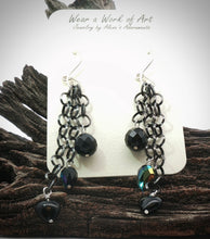 Load image into Gallery viewer, A pair of black and silver dangle earrings displayed on a white card labeled 'Wear a Work of Art Jewelry  resting on a piece of dark wood against a white background.