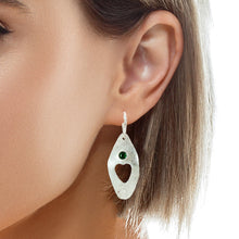 Load image into Gallery viewer, A close-up of a woman's ear wearing a textured silver dangle earring with a small green stone accent.