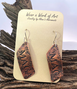 Copper earrings on a display card with 'Wear a Work of Art' text, against a natural wood background.