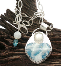 Load image into Gallery viewer, A silver pendant necklace displayed on a piece of dark wood. The pendant features a large heart-shaped blue and white plume agate and faceted moonstone