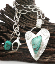 Load image into Gallery viewer, A sterling silver pendant necklace with a turquoise stone, displayed on a piece of dark wood. The necklace features a textured silver heart-shaped pendant with a central turquoise stone, a smaller round turquoise charm, and a textured silver clasp.