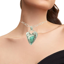 Load image into Gallery viewer, A silver heart-shaped pendant necklace with a turquoise center, shown worn on a model's neck against a white background.