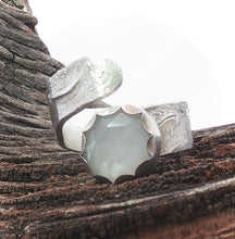 Load image into Gallery viewer, A sculptural silver ring with a faceted, moonstone gem photographed resting on textured tree bark against a bright white sky.