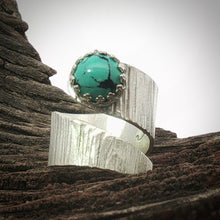 Load image into Gallery viewer, A silver ring with a large oval turquoise stone, photographed resting on textured dark wood against a bright white sky background.